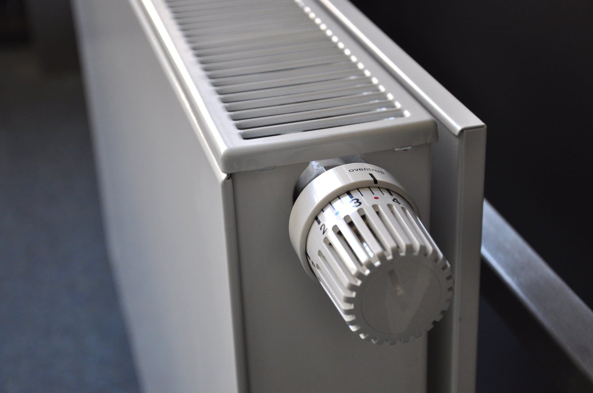 Radiateur panneau blanc vu de trois quarts, robinet thermostatique gradué de 1 à 5 monté en applique sur le côté