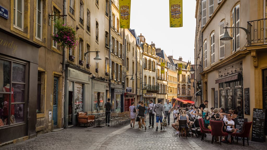 Rue pavée du centre ancien de Metz, façades en pierre de Jaumont et terrasses de café en fin de journée